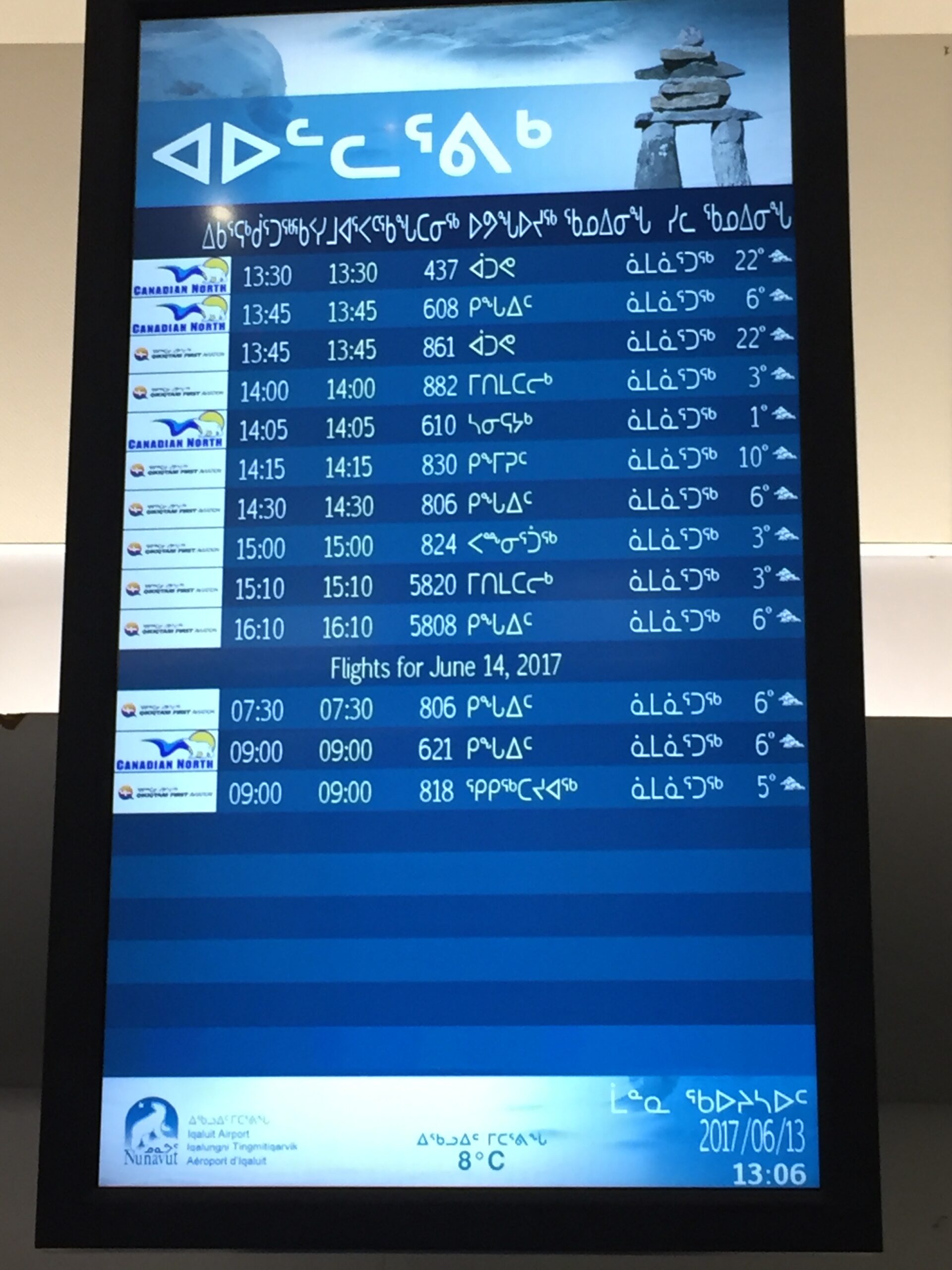 The airport flight listings on a screen in Iqaluit Airport in Nunavut Canada. The text is in Inuktitut.