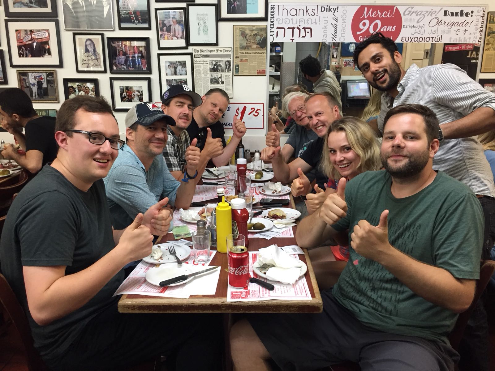 A group of a film crew sit together at a restaurant all giving the photographer a thumbs up